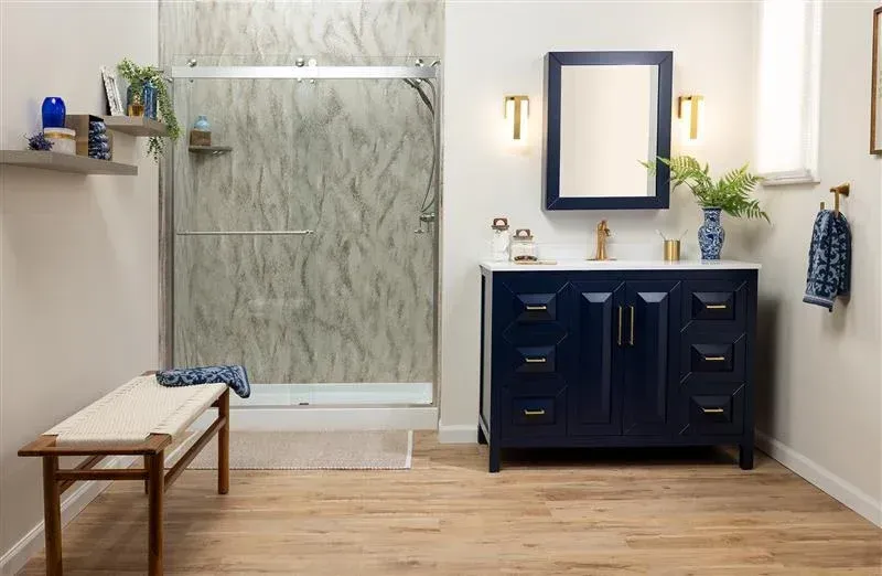 Modern bathroom with a navy vanity, mirror, wall lights, shower, and bench on wood flooring