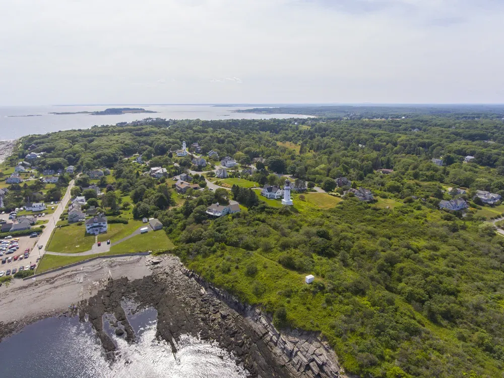 Aerial view of a rocky coastline with green trees, houses, and ocean waves