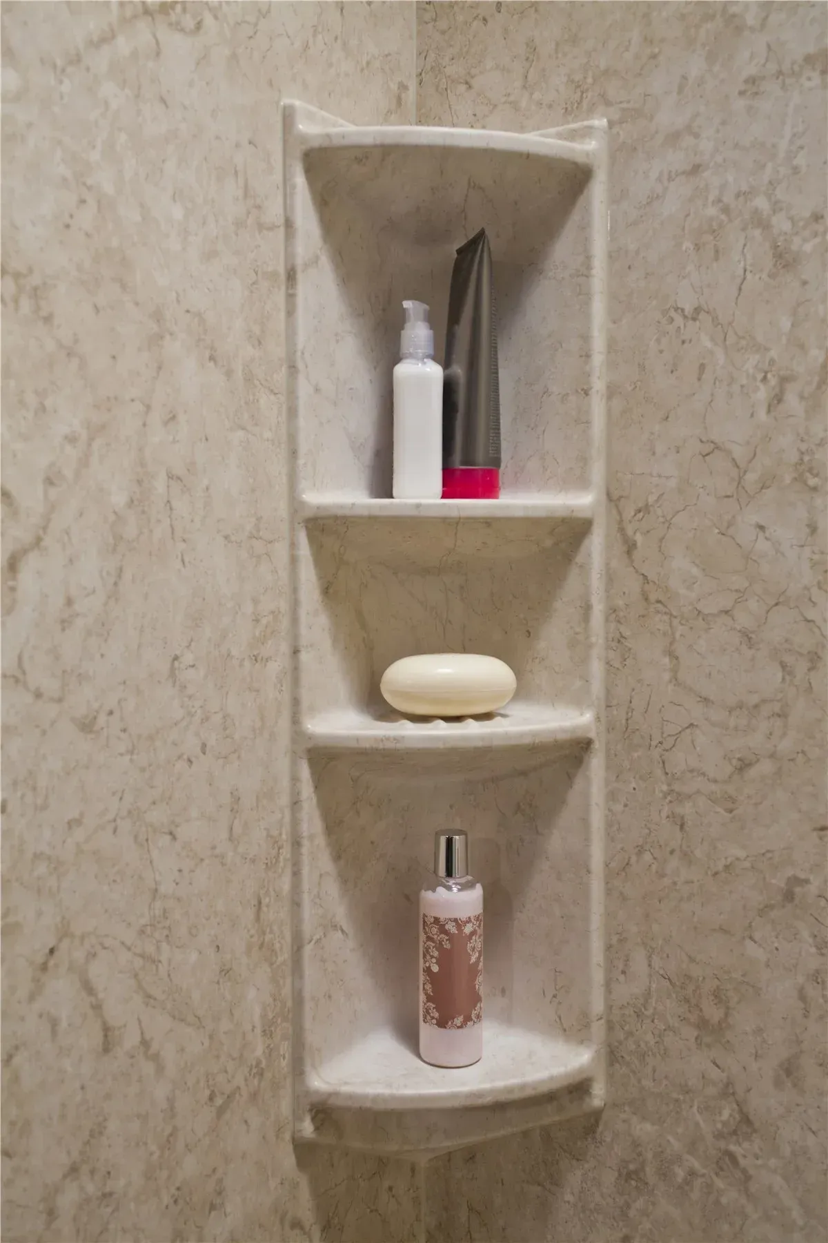 Wall niche with bath items: white bottle, metal tool, soap, and pink perfume bottle on beige marble shelves