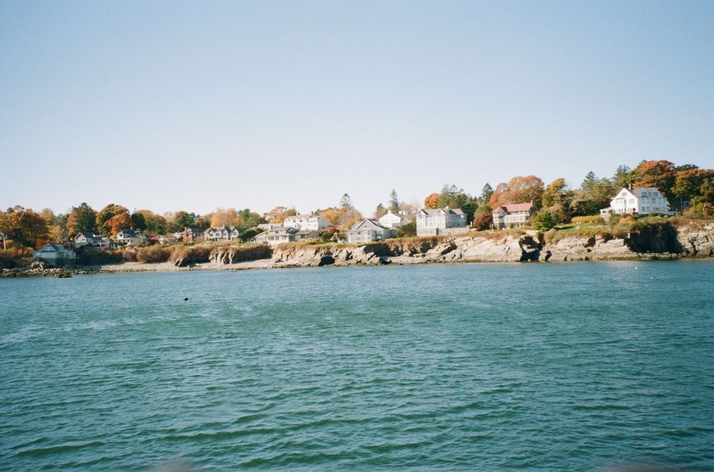 Coastal shoreline with houses on rocky cliffs above calm blue water under a clear sky