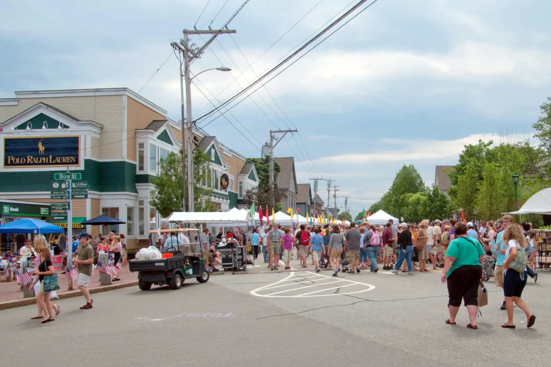 Crowded street festival with tents, people walking, and shops on a sunny day