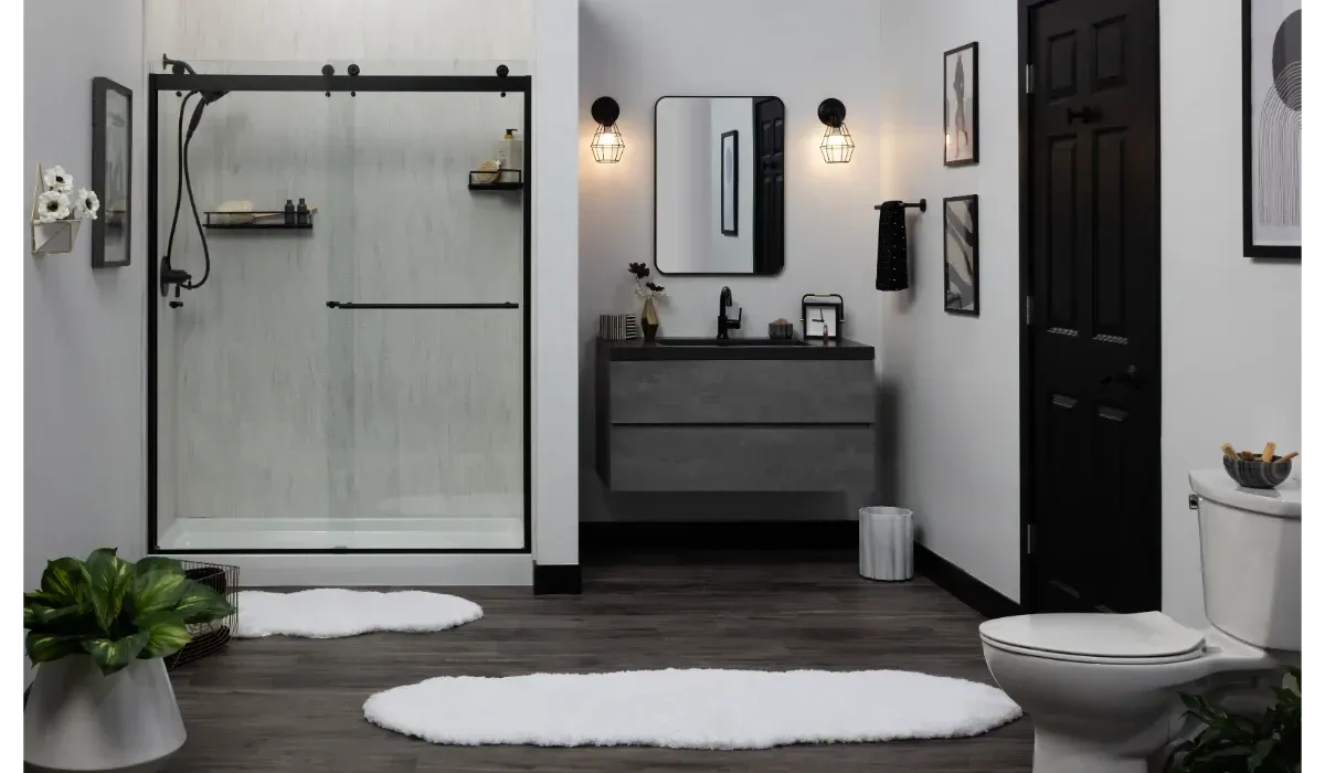 Modern bathroom with walk-in shower, vanity, black door, white rugs, and potted plants.