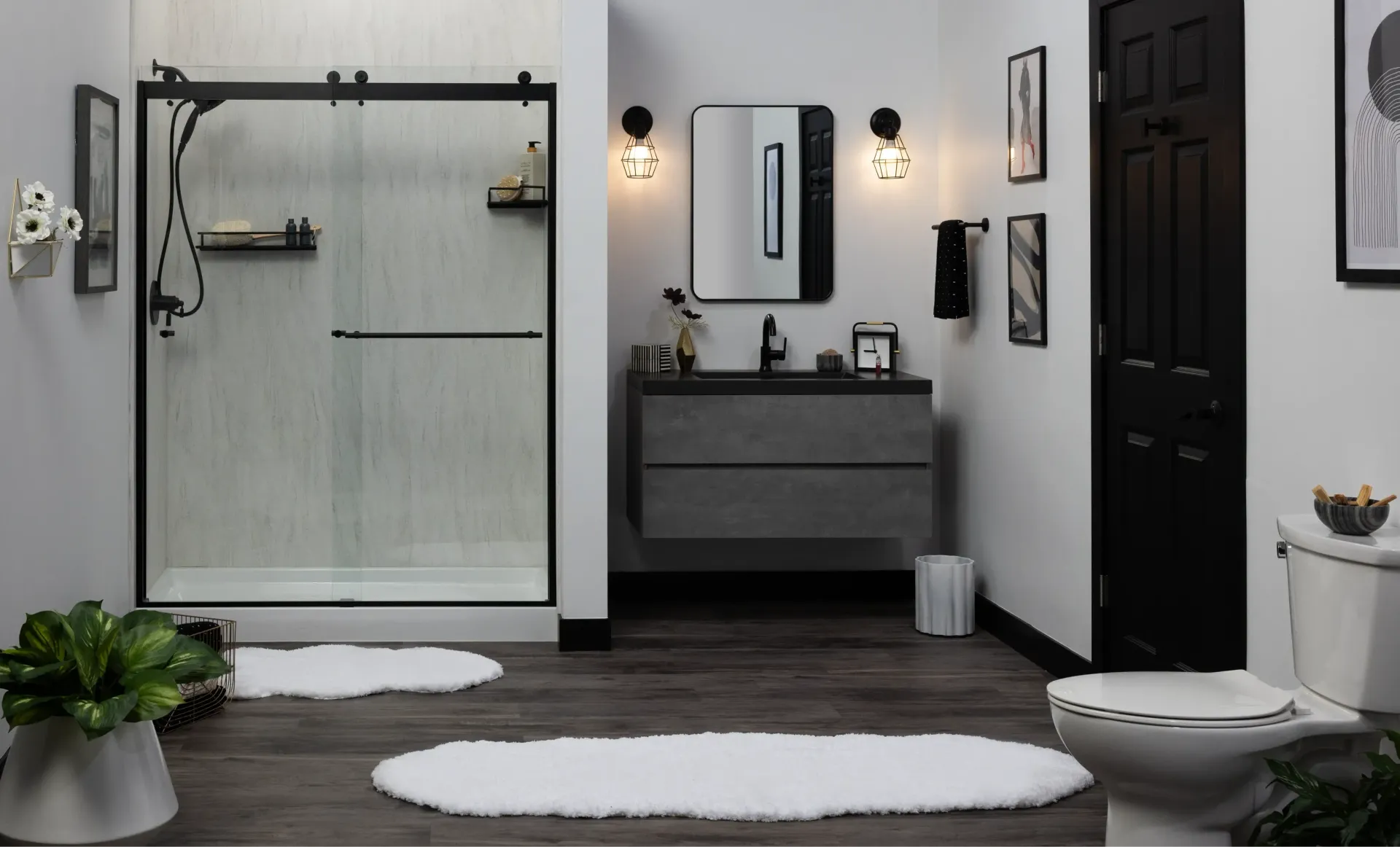 Modern bathroom with walk-in shower, vanity, black door, and white rugs on dark flooring