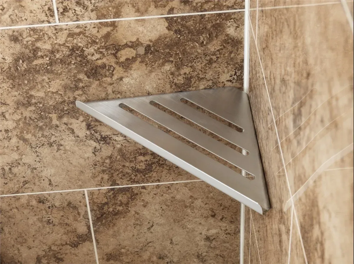 Corner shower shelf with a silver triangular metal drain grate on beige tile wall