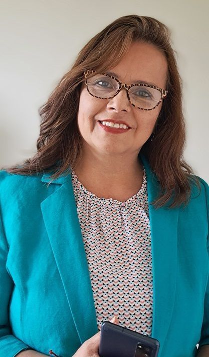 Una mujer que lleva gafas y una chaqueta azul sostiene un teléfono móvil.