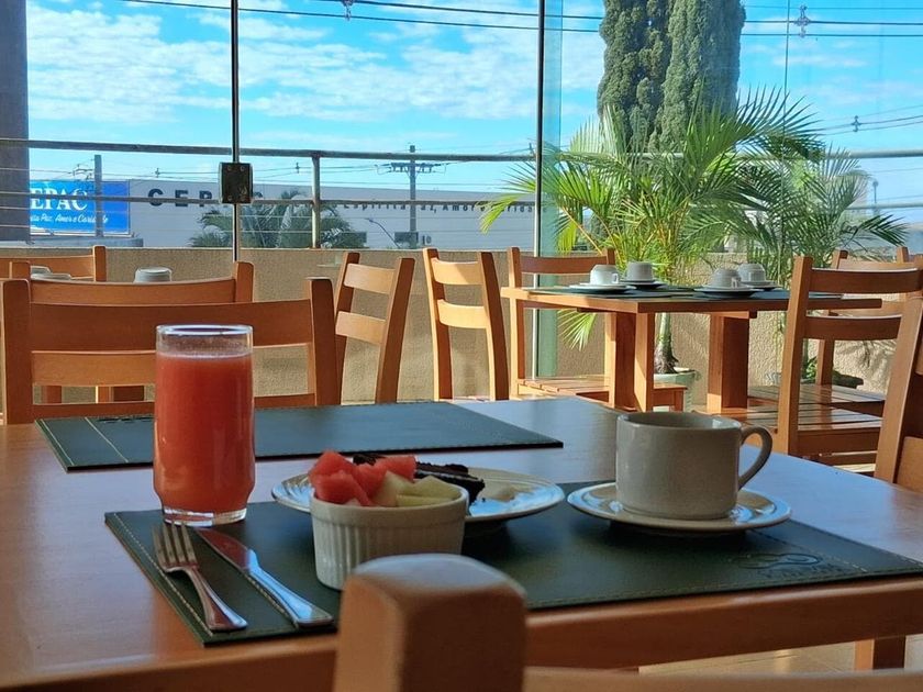 Mesa de café ao ar livre, ensolarada, com suco, café e uma sobremesa de morango, sobre cadeiras de madeira junto à janela
