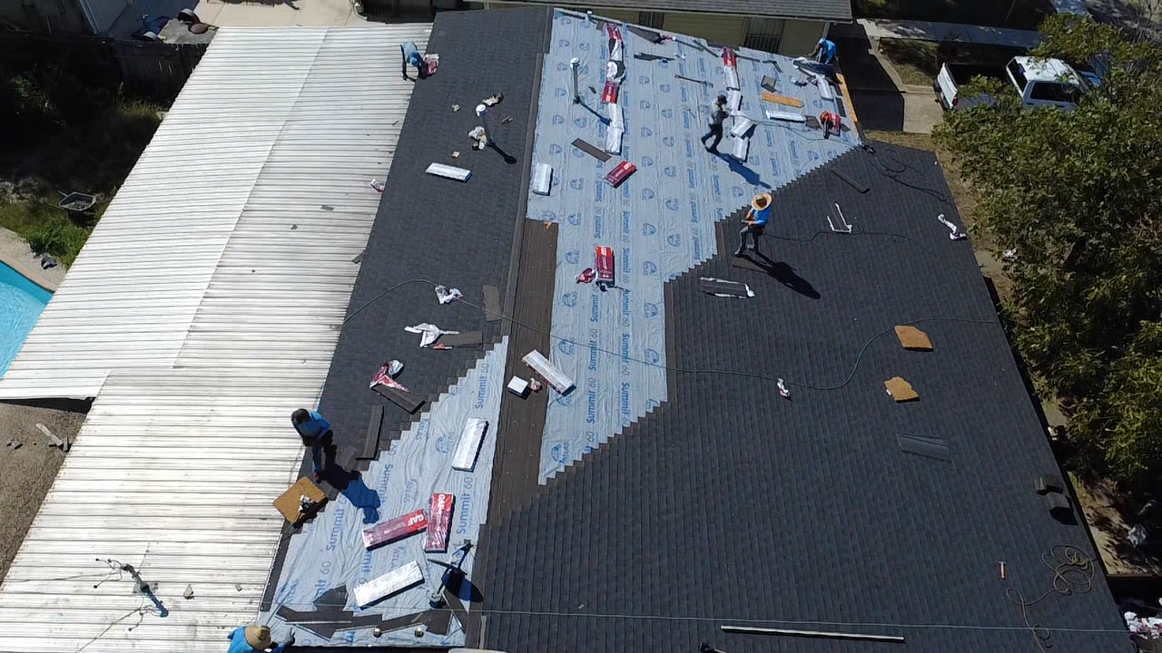 Two workers install a metal pole into the ground. One leans over it, while the other pulls a lever.