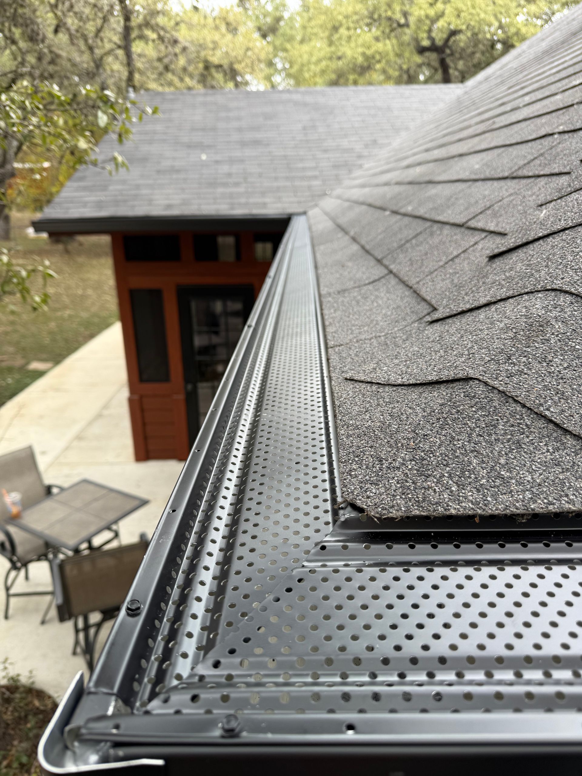 Roofer in orange hardhat and safety vest, working on a gutter on a sunny day.
