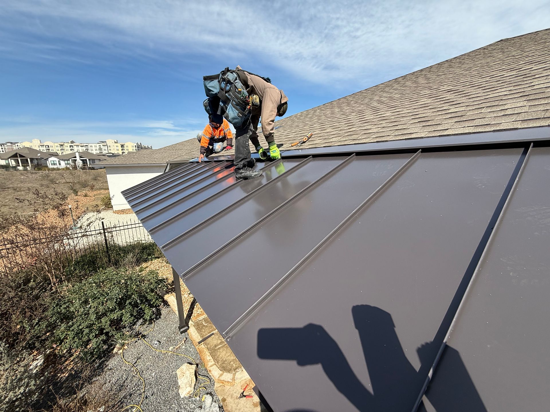 Roofers installing shingles on a roof under a blue sky.