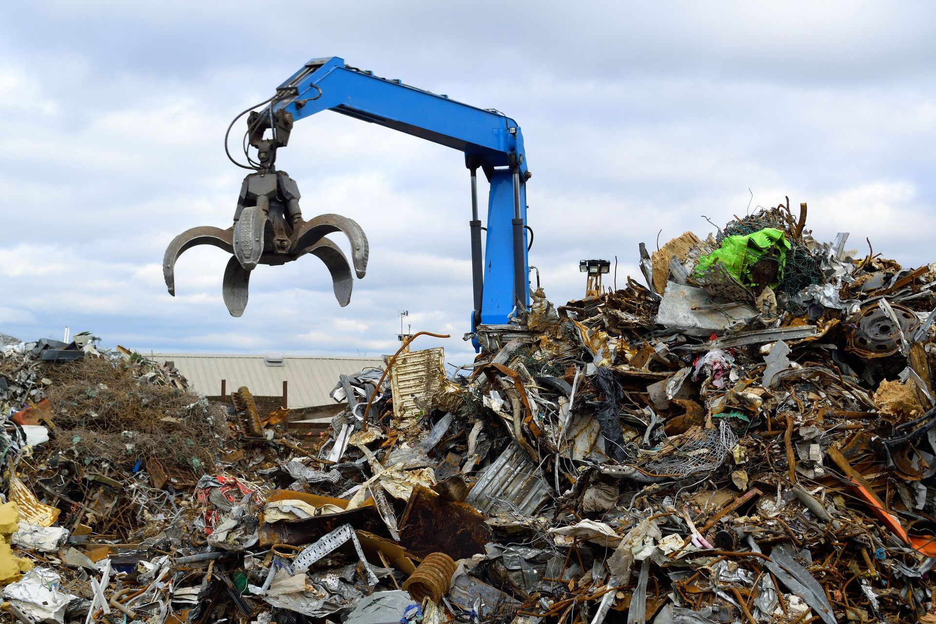 Blue hydraulic Clow Crane used for picking up scrap metal at recycling yard.