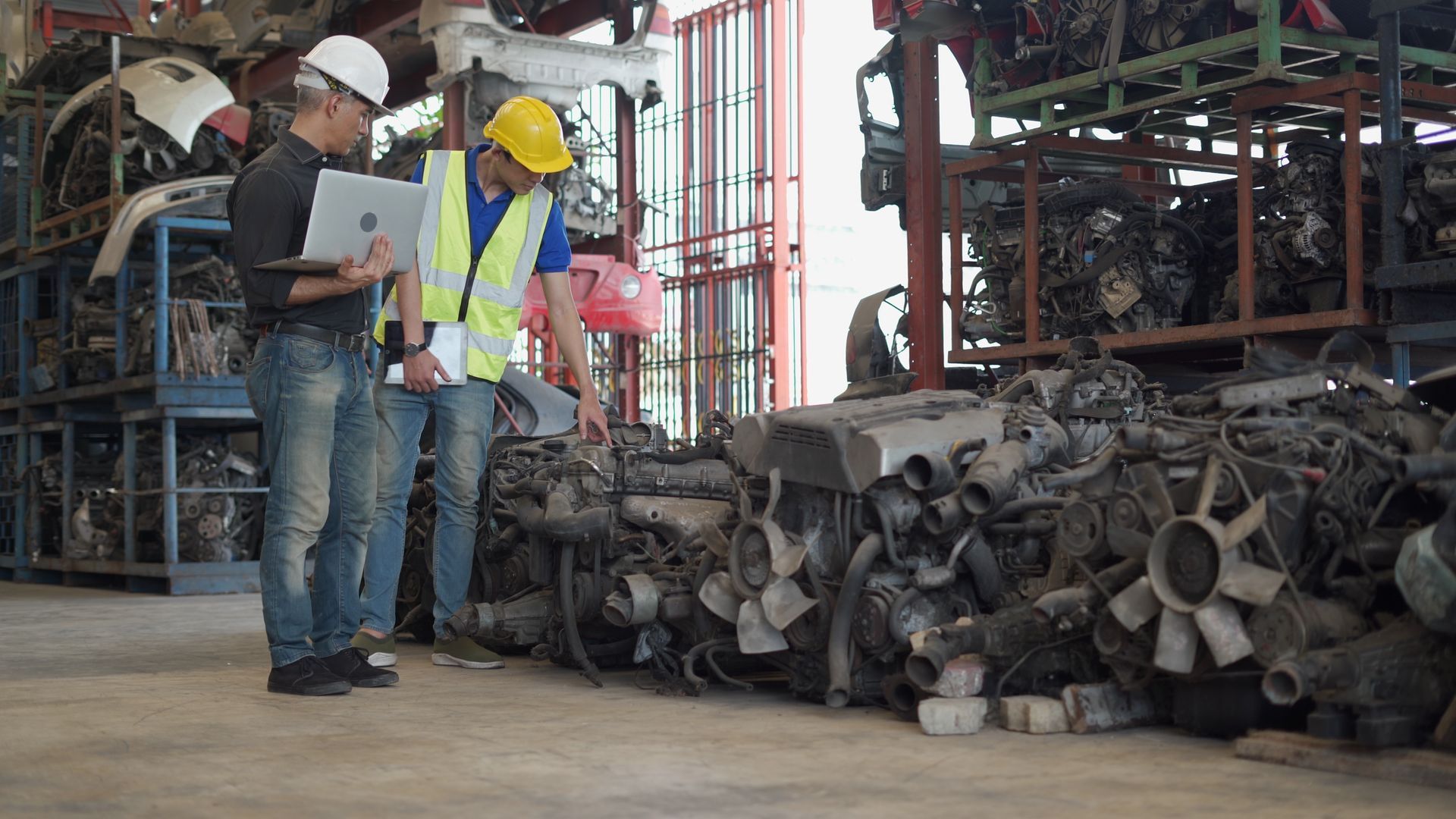 Workers inspecting automotive scrap metal parts and engine components at a commercial scrap metal ya
