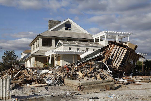 House with significant damage from a disaster; debris piles up in front.