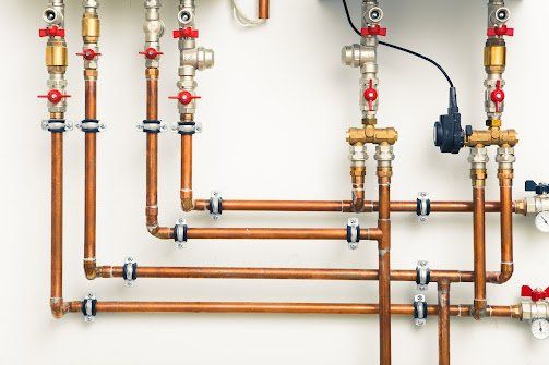 Copper pipes with red and brass valves against a white wall.
