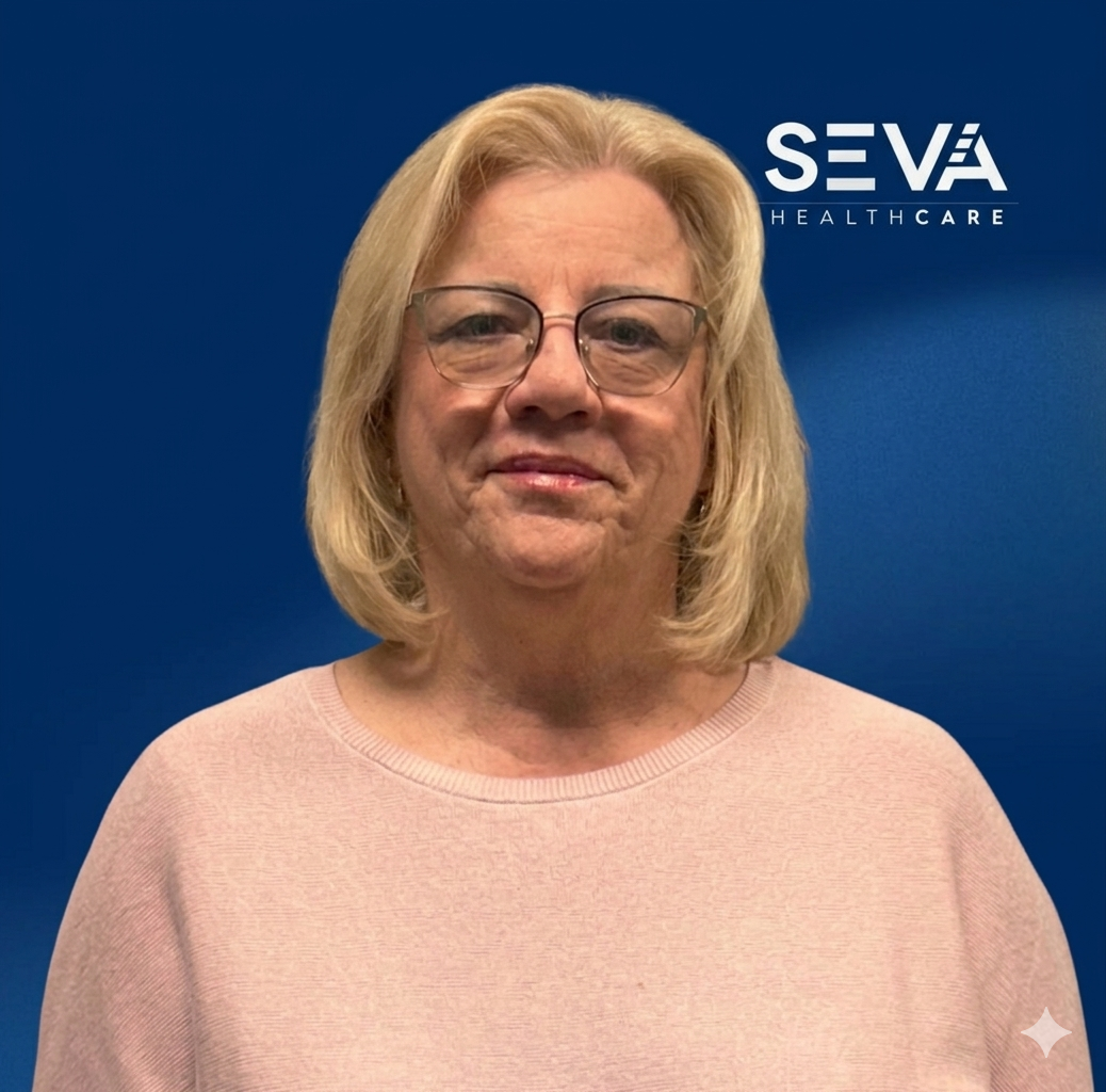 Portrait of a person in glasses wearing a pink sweater against a blue SEVA Healthcare backdrop