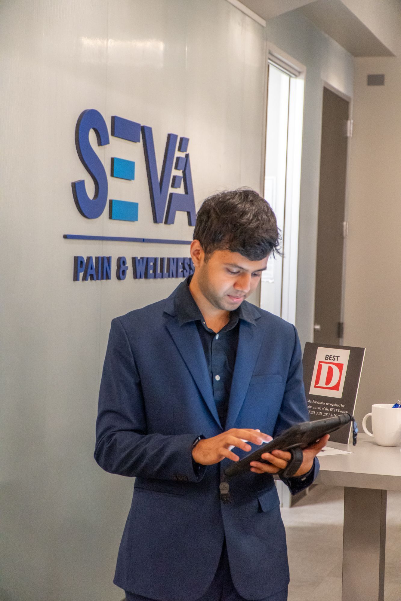 Man in a blue blazer using a tablet in a modern office lobby with SEVA signage