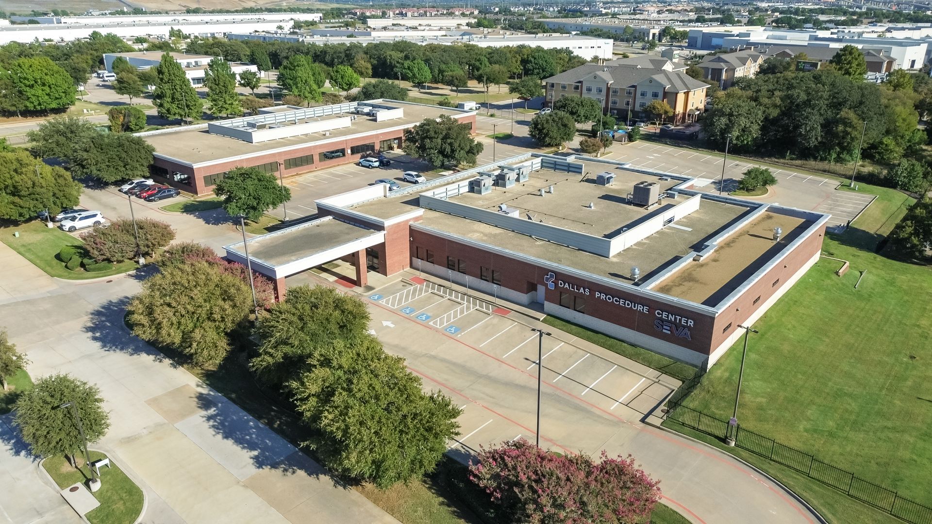 Aerial view of a school campus with brick buildings, tennis courts, trees, and parking lots