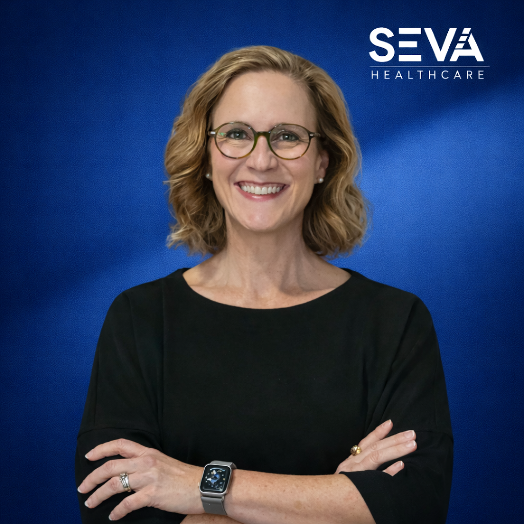 Smiling person in black shirt with glasses, arms crossed, against blue SEVA Healthcare backdrop