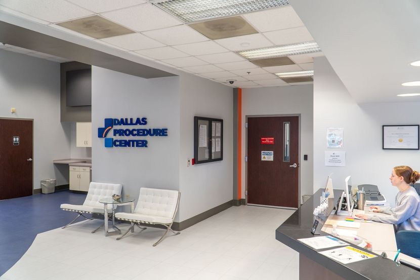Hospital procedure center waiting area with chairs, reception desk, and a staff member at a computer