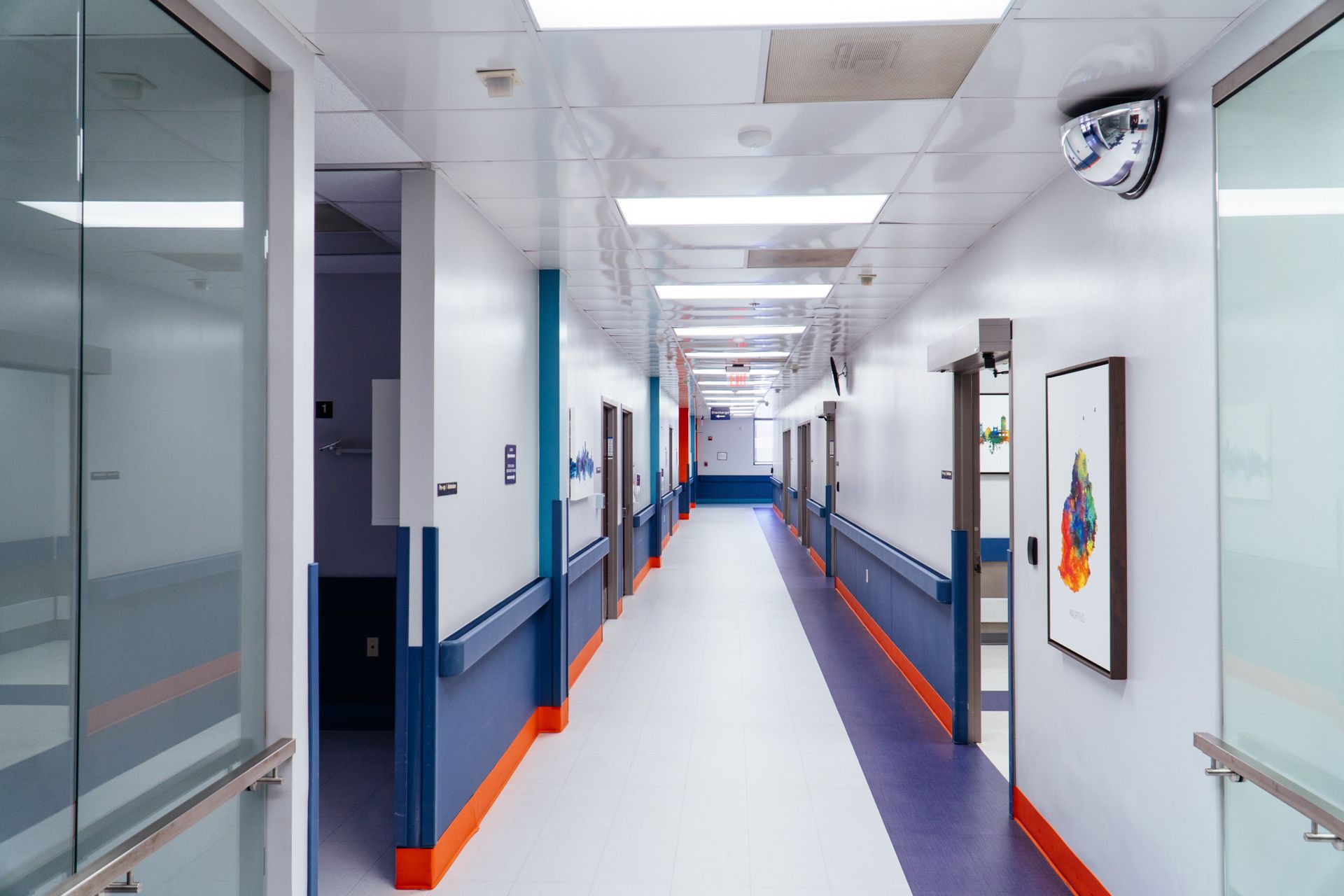 Bright, empty hospital corridor with white walls, blue trim, and orange floor accents
