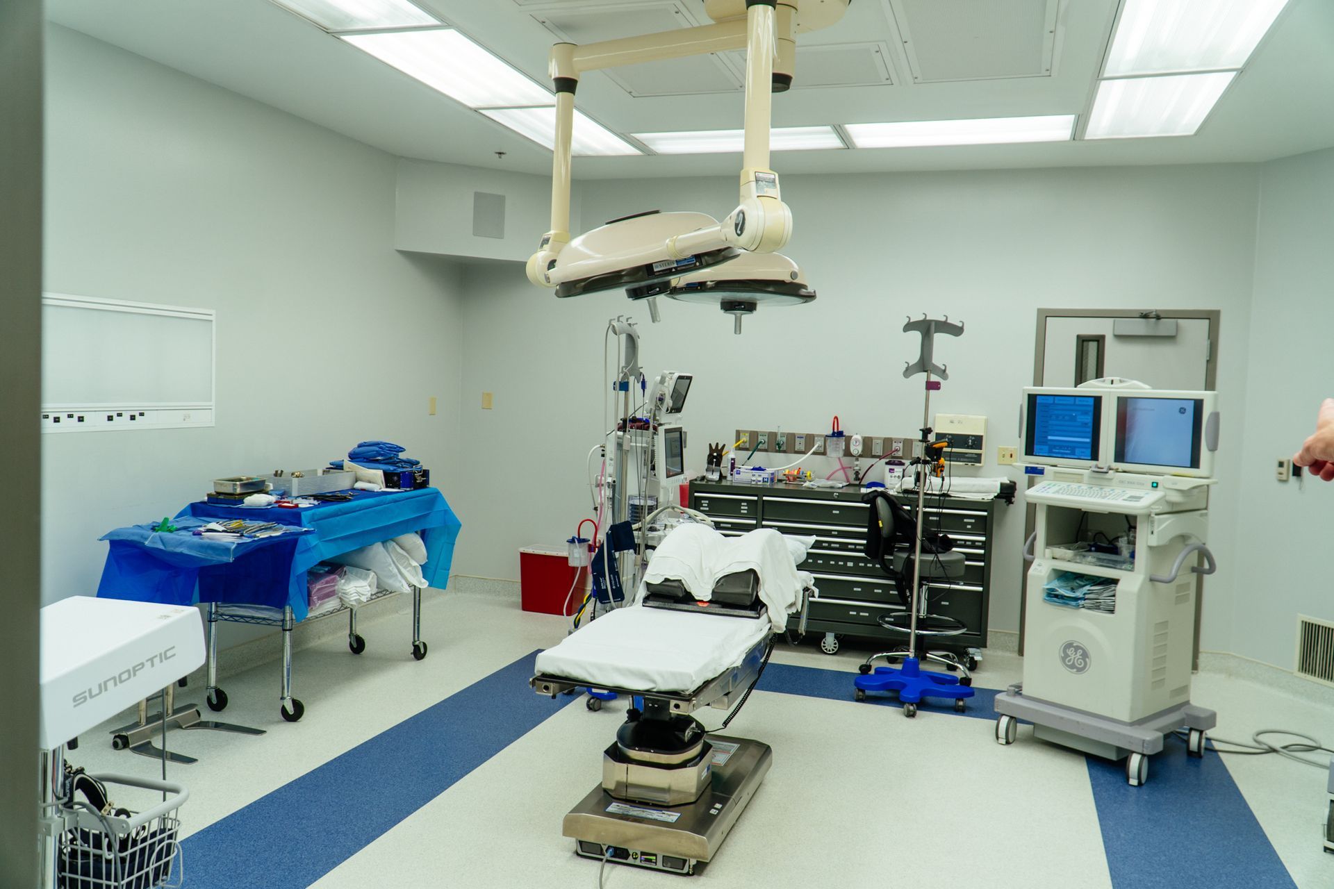Empty operating room with surgical table, overhead light, and medical equipment monitors.