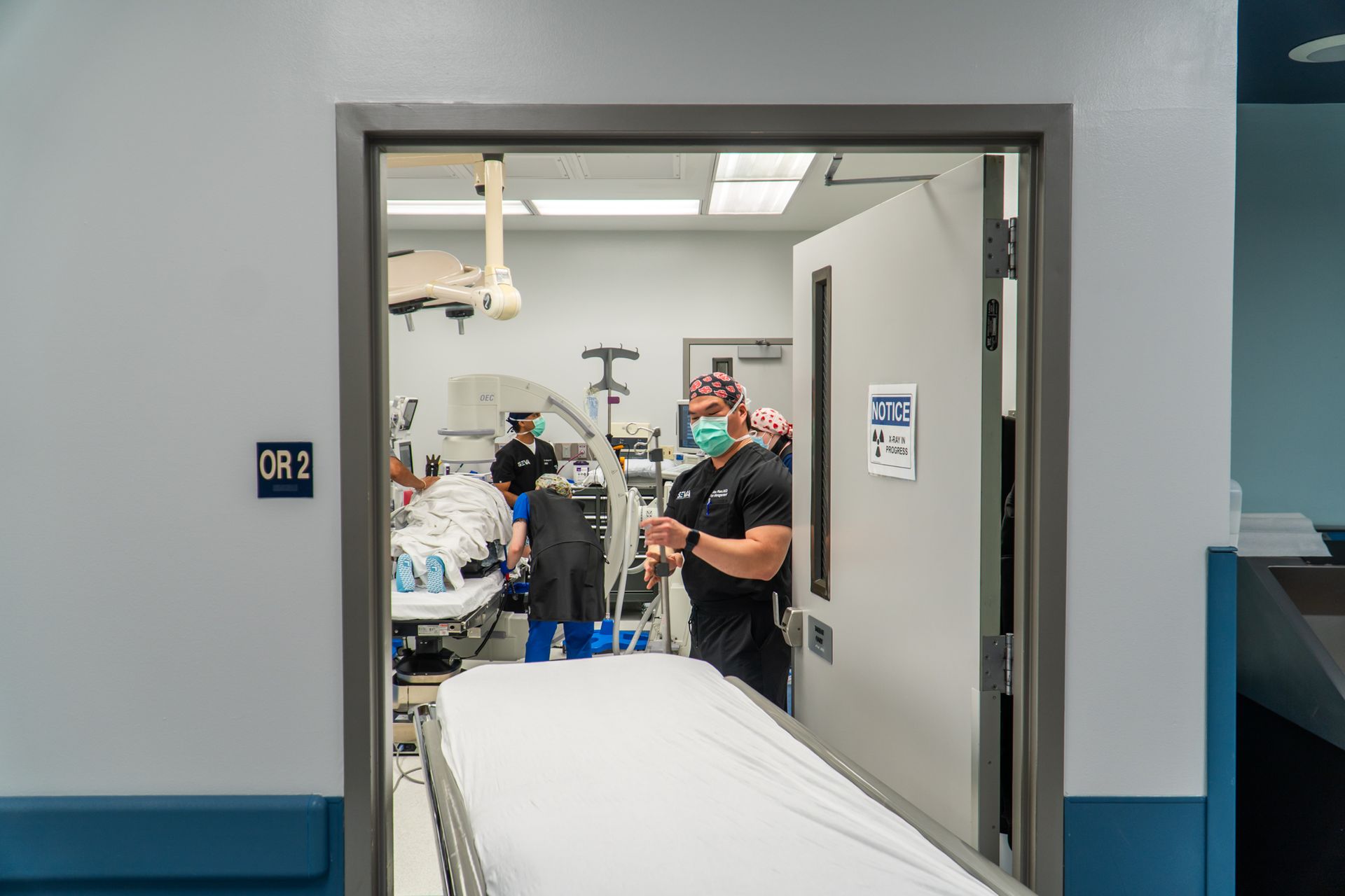 Hospital room doorway with medical staff around a patient bed and equipment