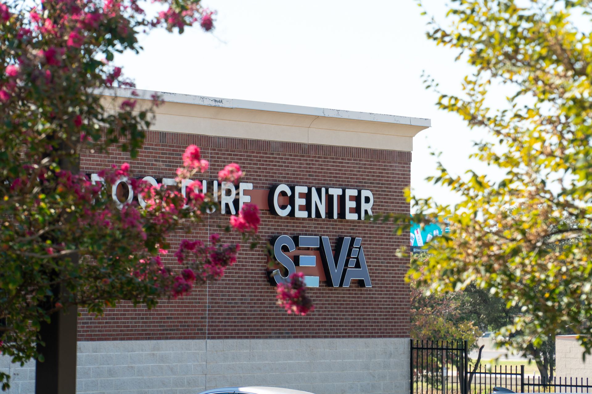 SEVA office center sign on a brick building, framed by flowering trees