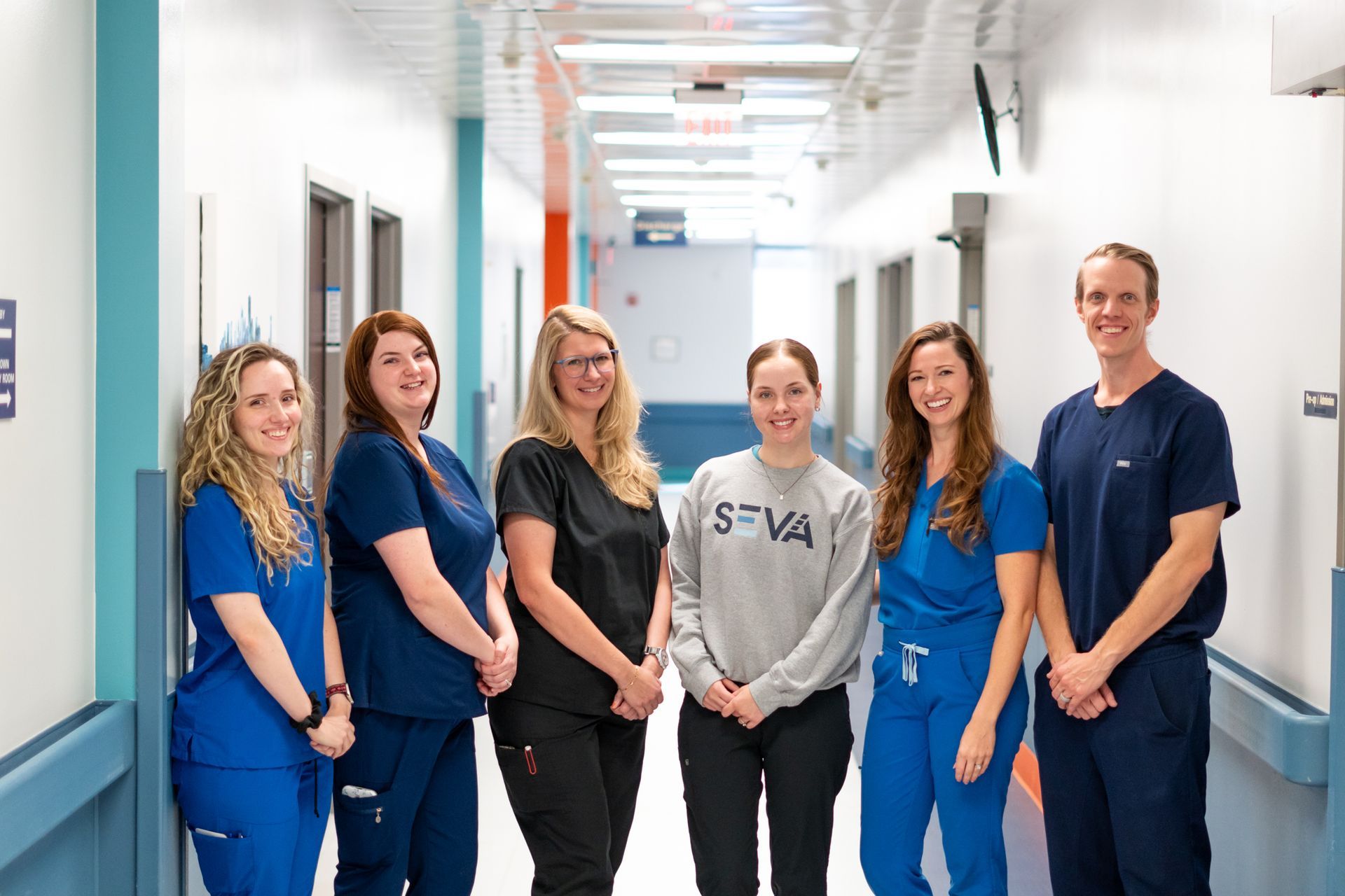 Seva Healthcare workers standing in a bright hospital corridor, smiling at the camera.