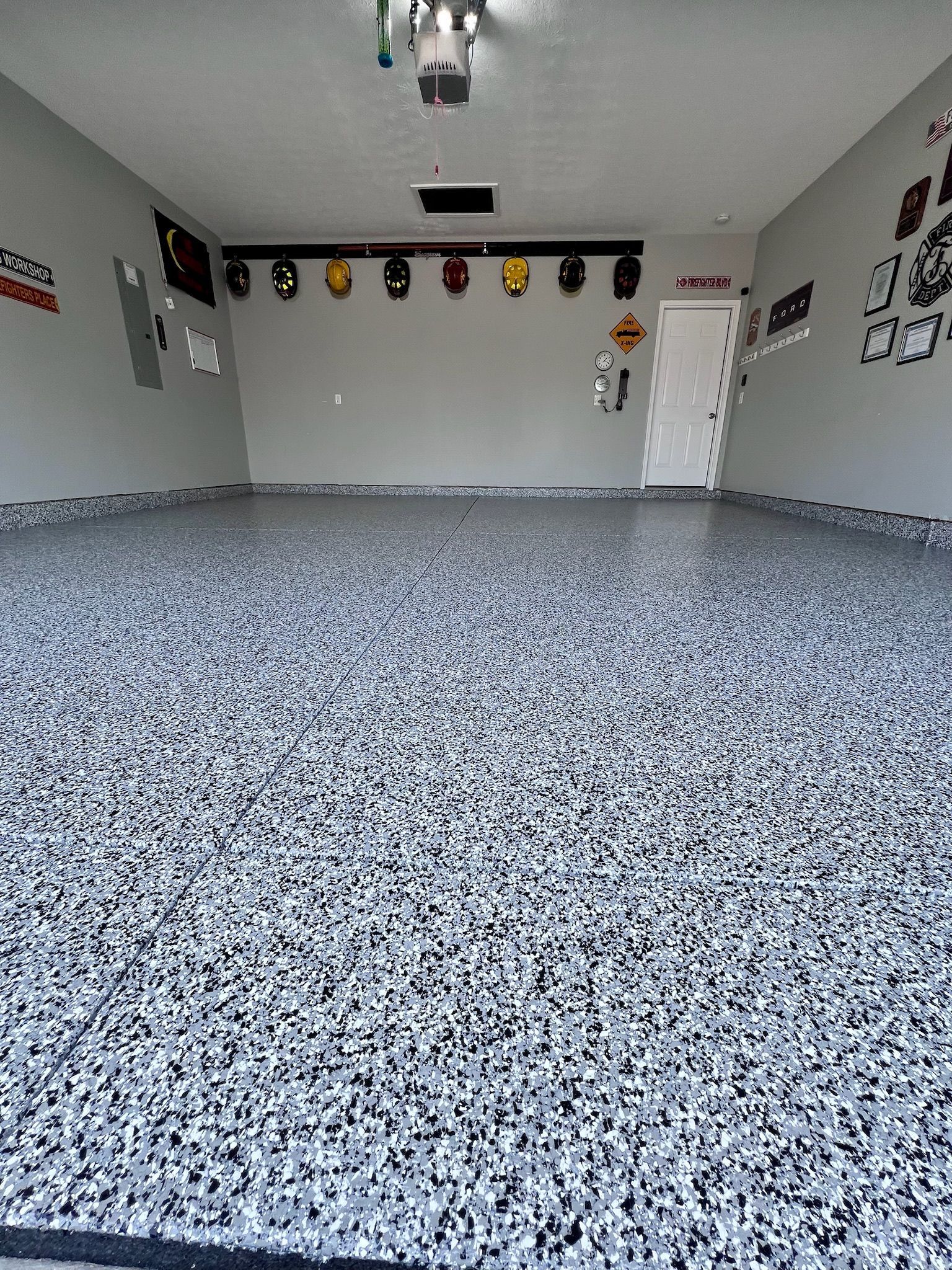 Garage with gray and black speckled epoxy floor, gray walls, decorations, and a white door.