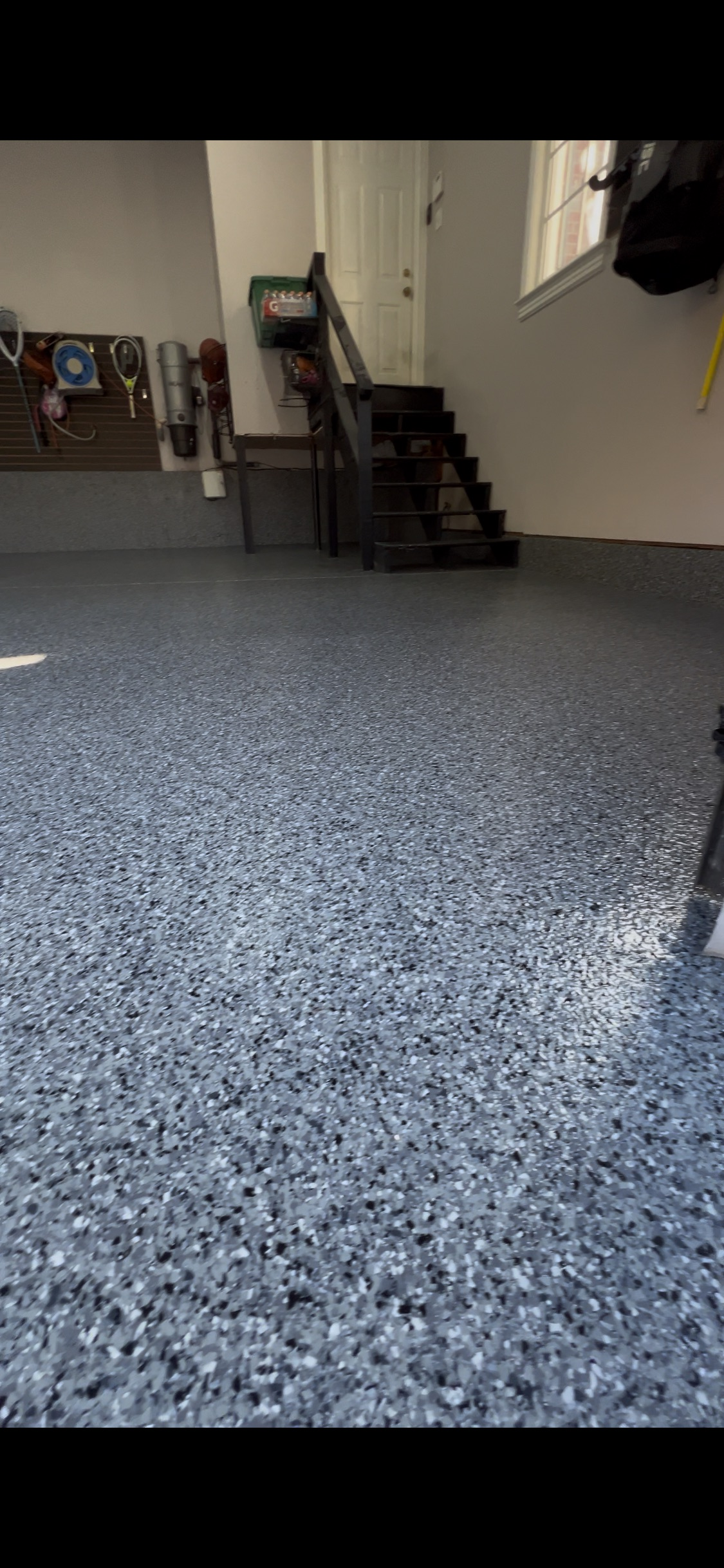 Garage with dark gray speckled epoxy floor and stairs leading up.