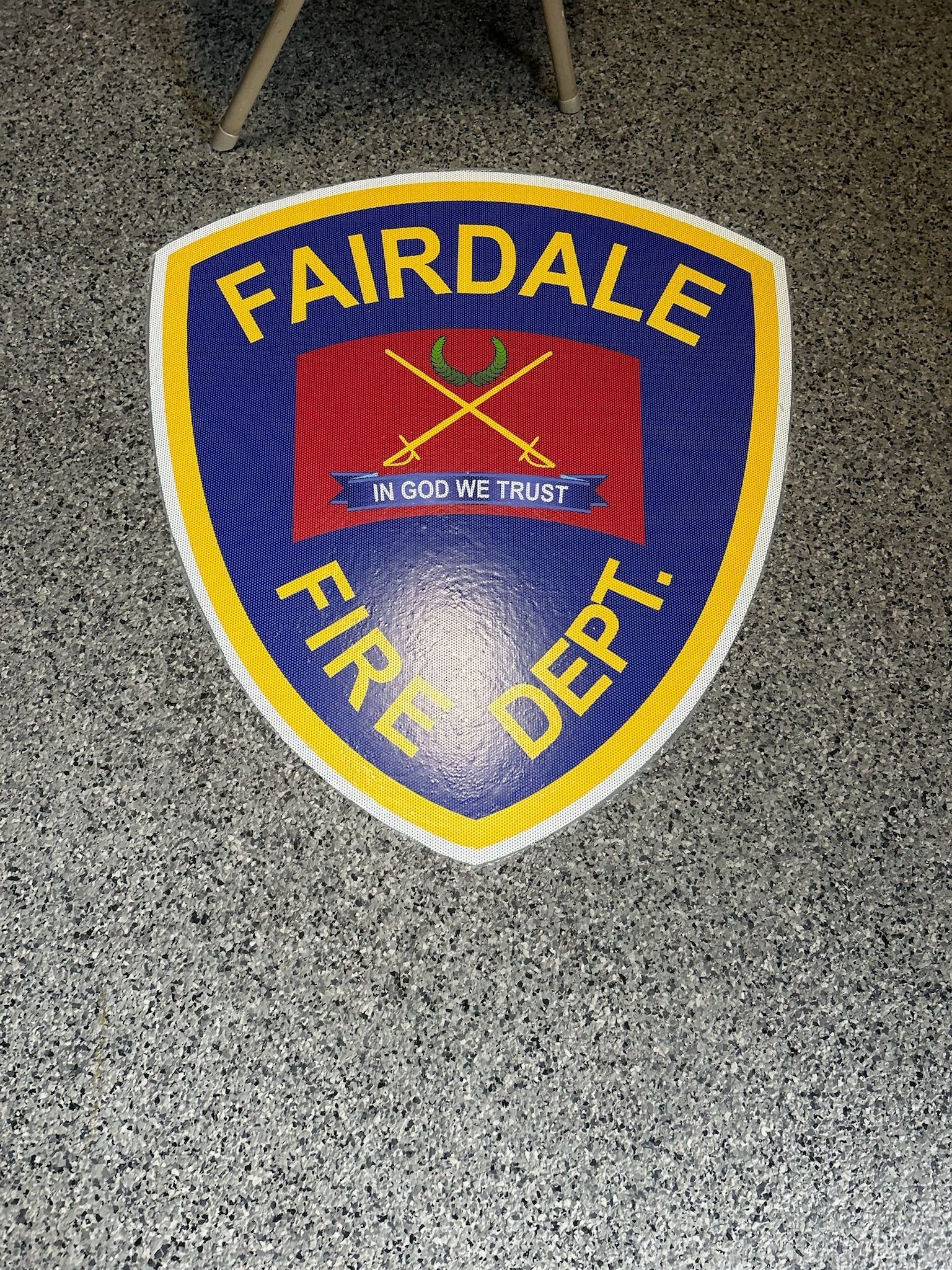Fairdale Fire Dept. emblem on speckled floor. Blue, yellow, and red shield with crossed axes and text.