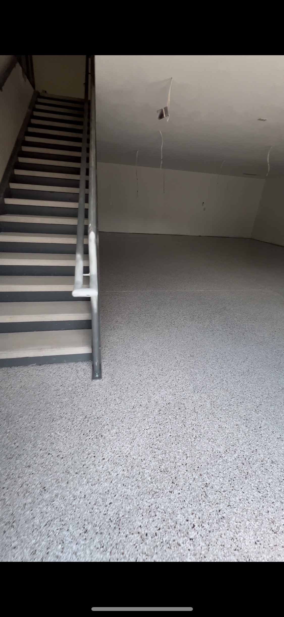 A gray staircase with a metal railing is inside of a room with a speckled floor.