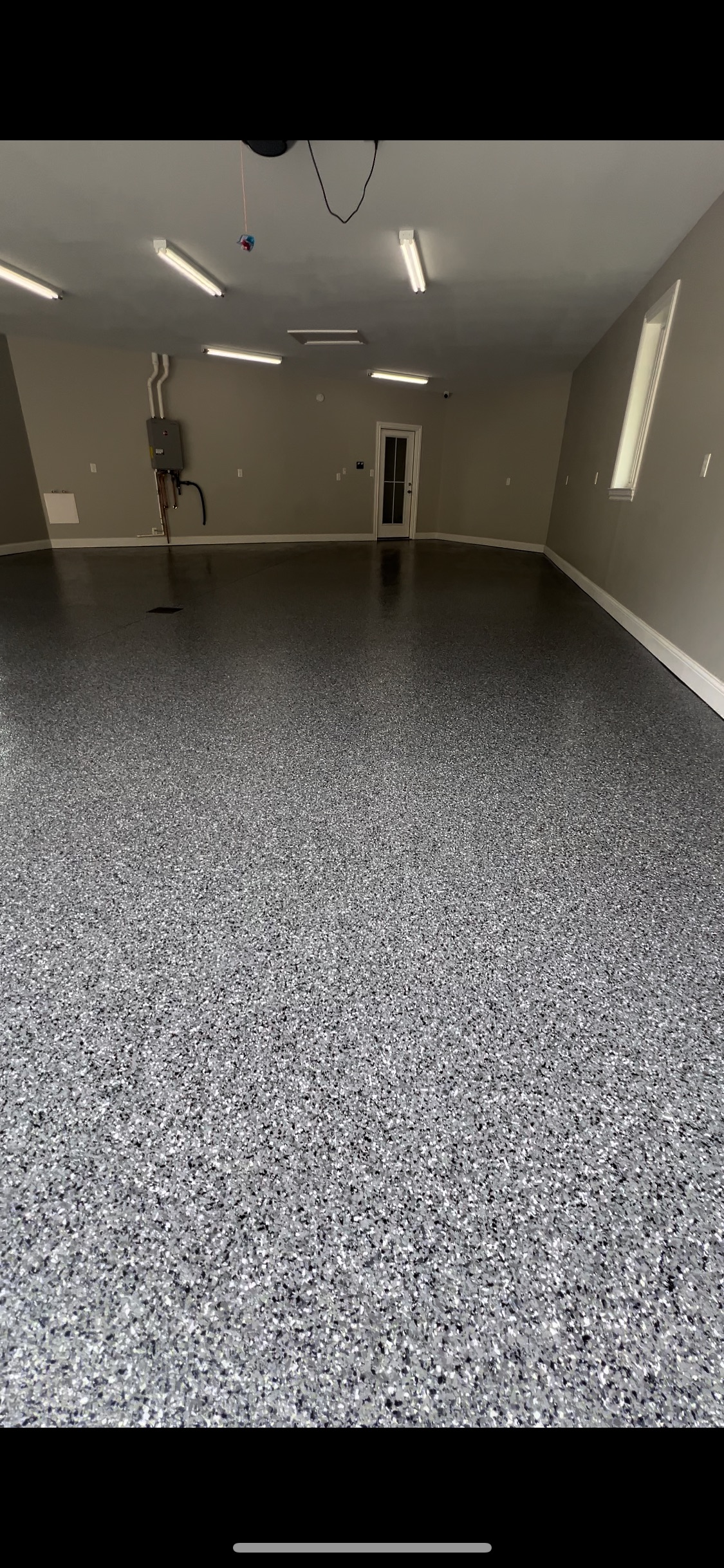 A newly coated garage floor with epoxy. Walls are light brown. Fluorescent lights are on the ceiling.