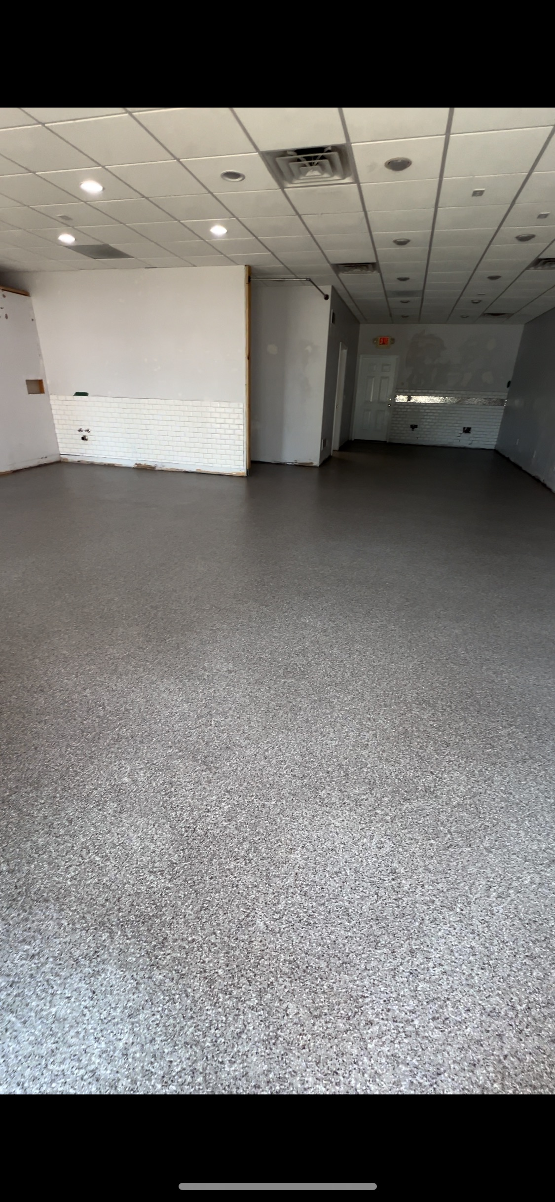 An empty retail space with a speckled floor, white walls, and a dropped ceiling.