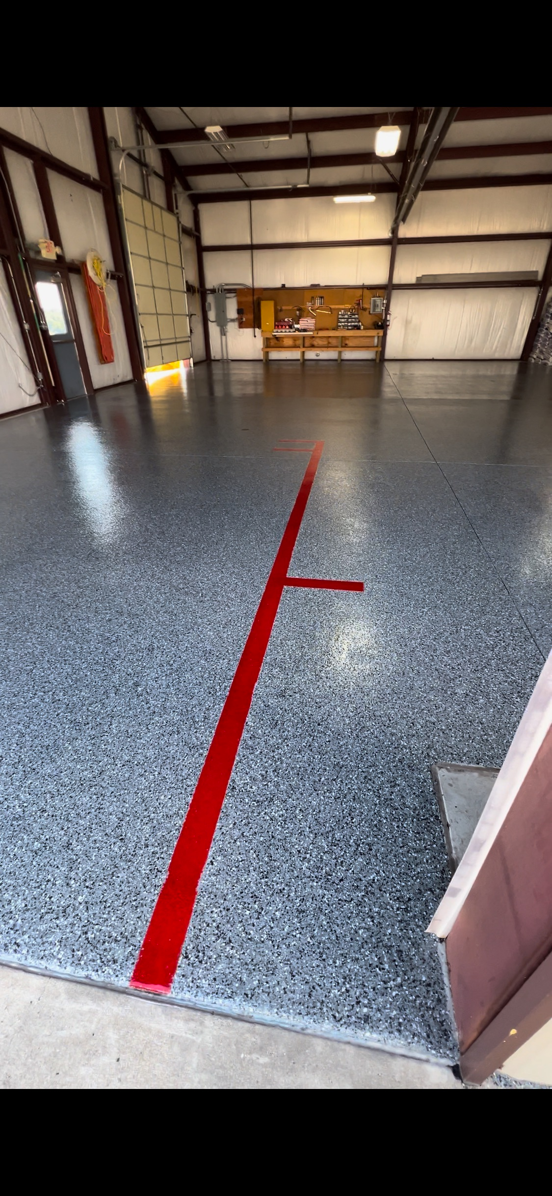 Red line painted on a shiny, speckled gray floor inside an open warehouse.