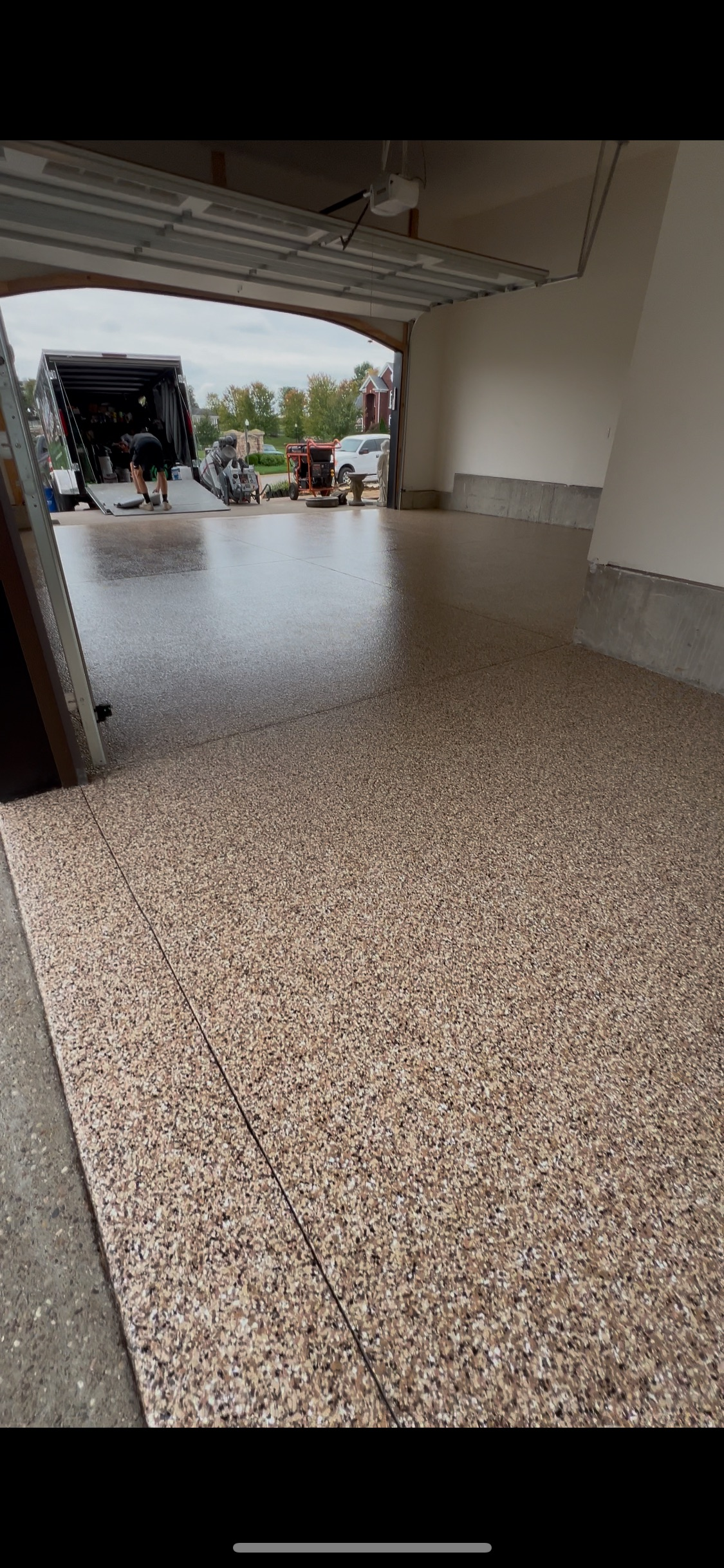 A garage with a new speckled epoxy floor. The garage door is open, showing a truck and outdoor scenery.