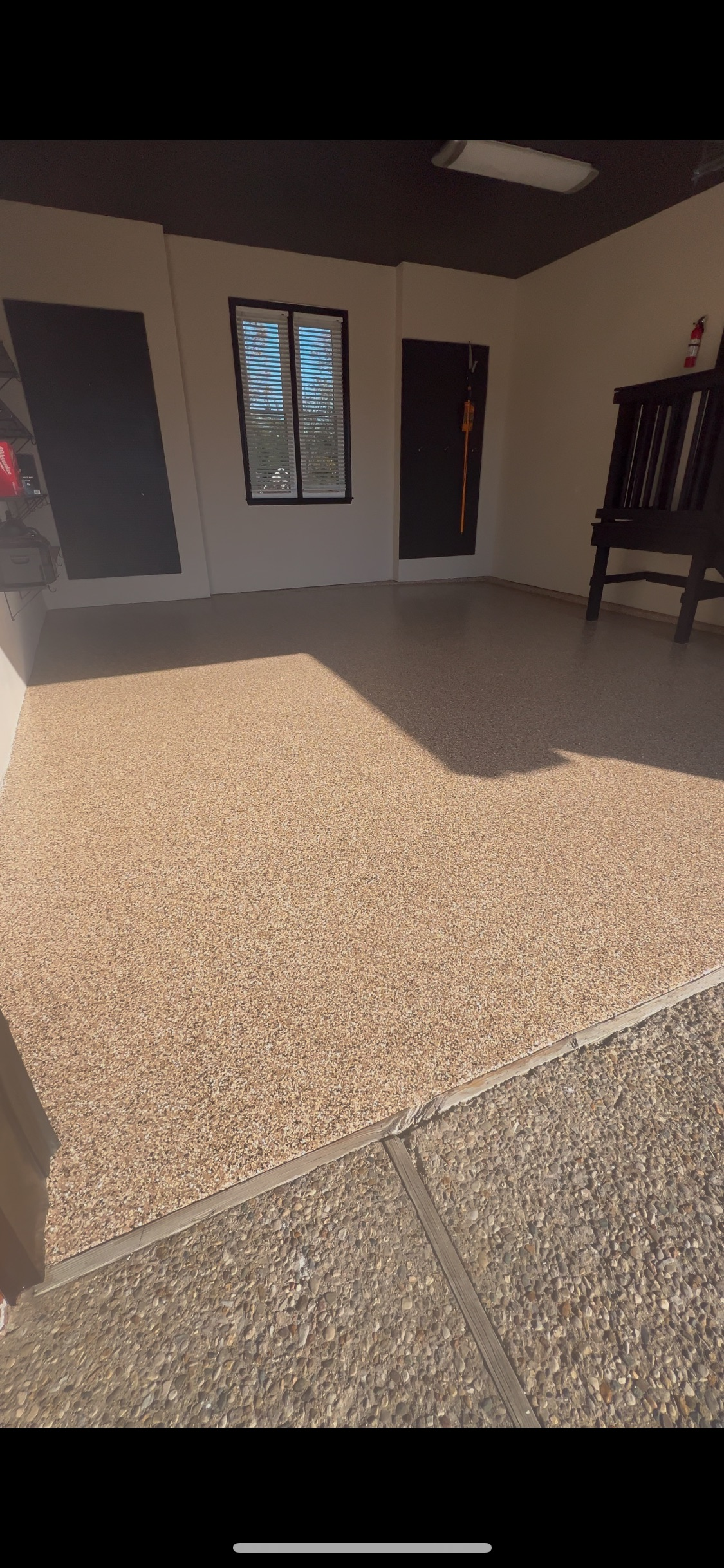 A covered patio with a pebble floor, a window, a dark door, and a wooden chair.