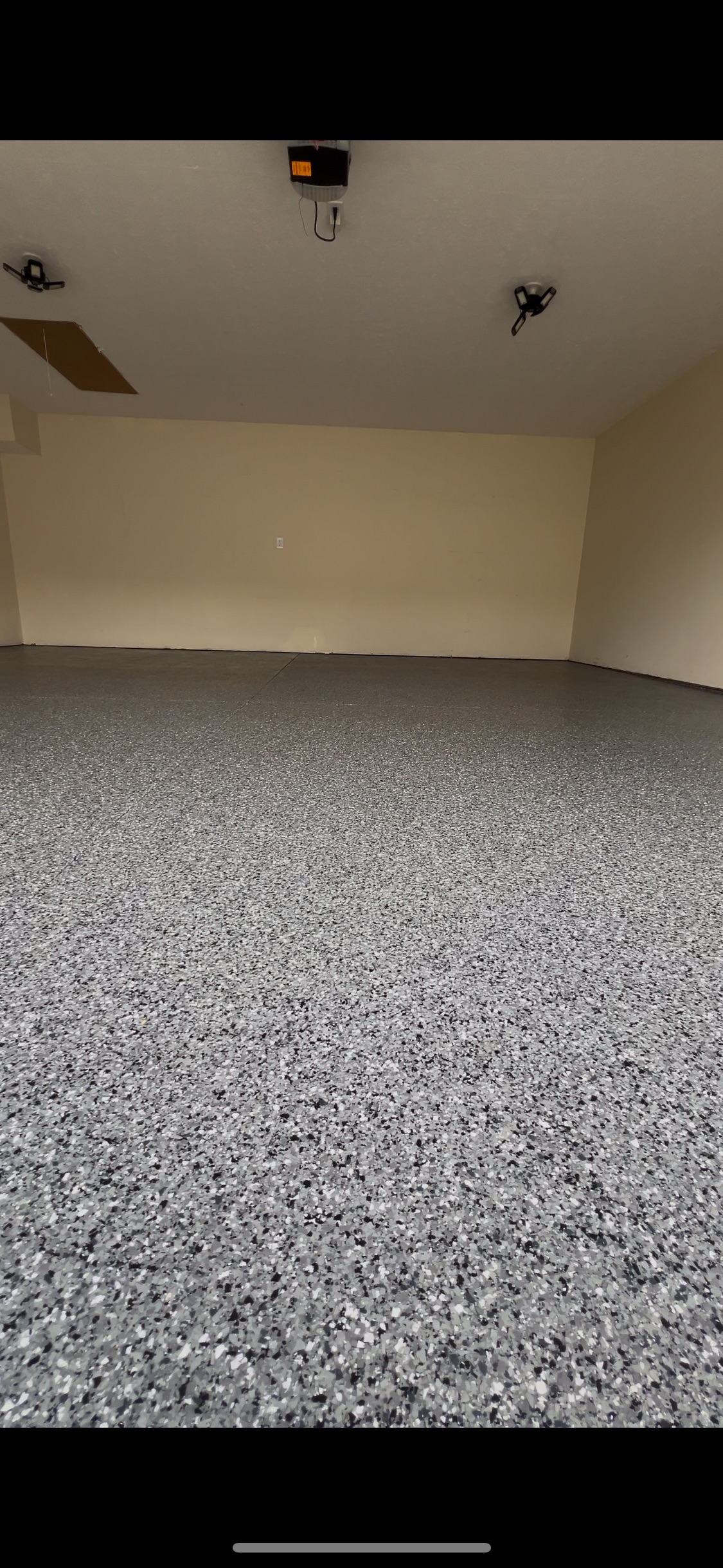 An empty, beige-walled room with a speckled gray floor and overhead lights.