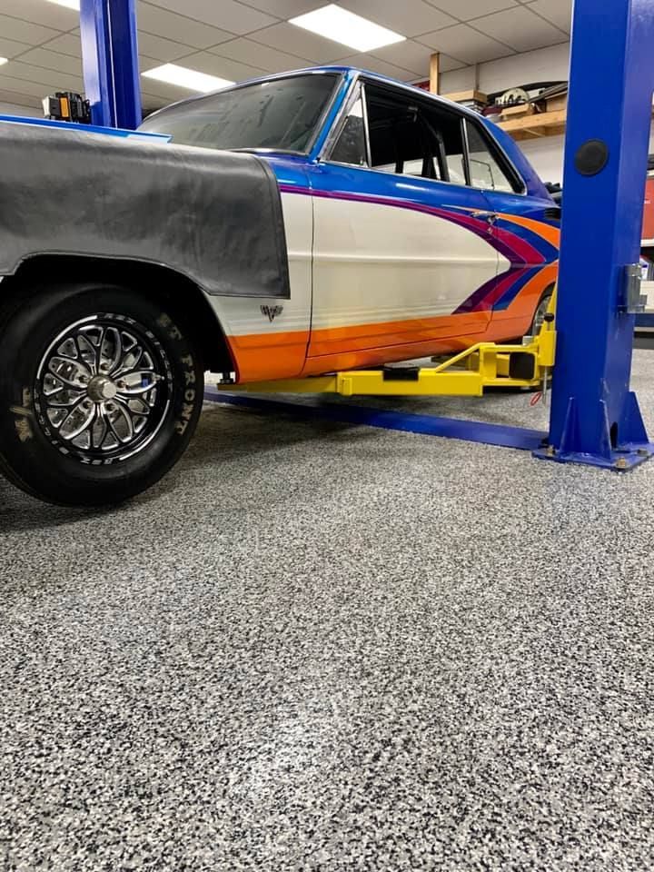 A classic car with custom paint is raised on a lift inside a garage.