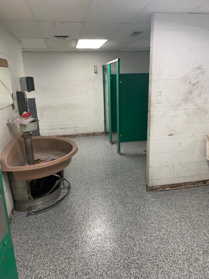 Public restroom with a large sink, green stall doors, and gray speckled flooring.