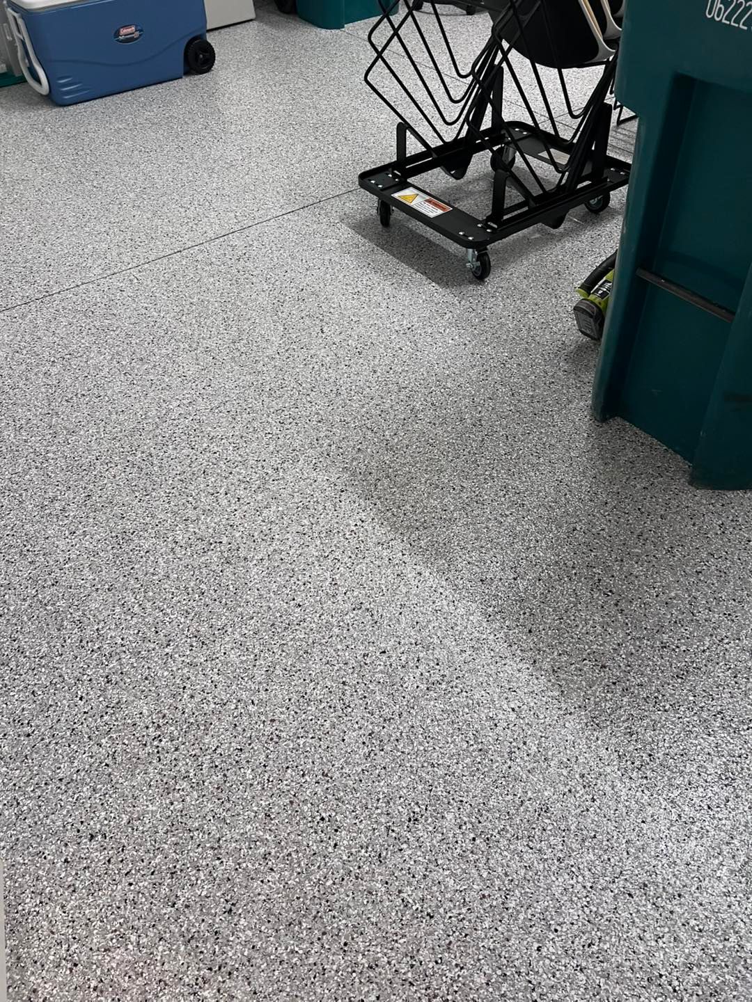 Epoxy-coated garage floor with gray, black, and white flecks. Blue storage container and equipment cart in the background.