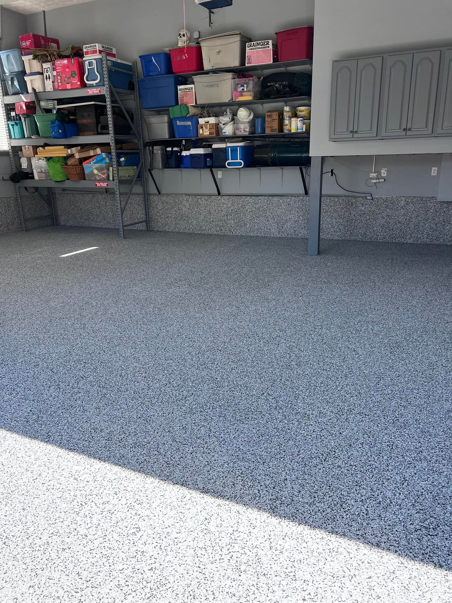 Garage with epoxy flooring, metal shelving, and cabinets filled with storage boxes and various items.