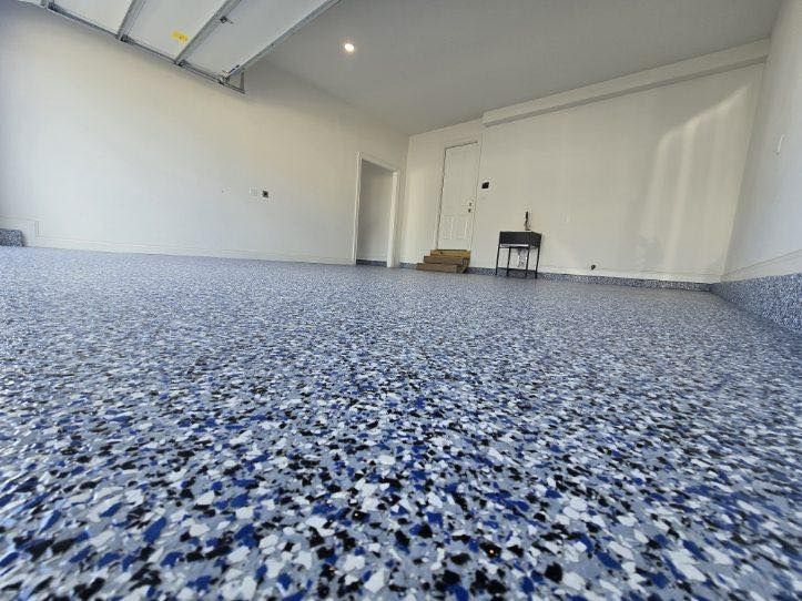 Blue and white speckled epoxy floor in an empty garage with white walls.