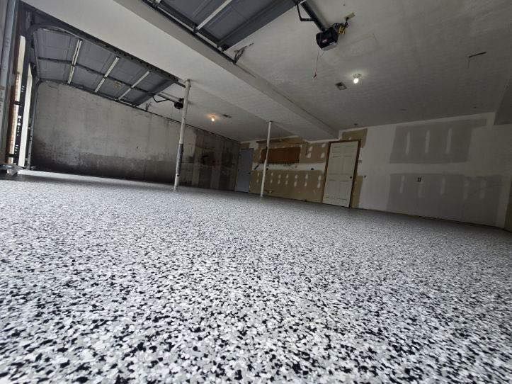 Garage with a speckled gray epoxy floor, open garage door, unfinished walls.