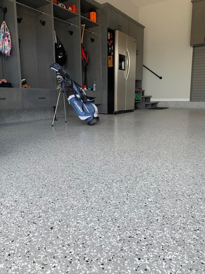 Garage with gray speckled floor, built-in lockers, and a golf bag. A refrigerator stands nearby.