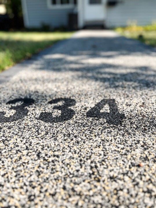 Painted house number 434 on a sunlit gravel walkway with blurred grass and a house in the background