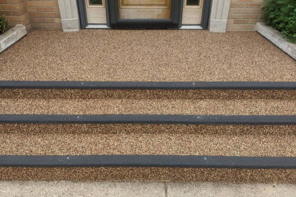 Three gravel-textured front steps leading to a glass entry door