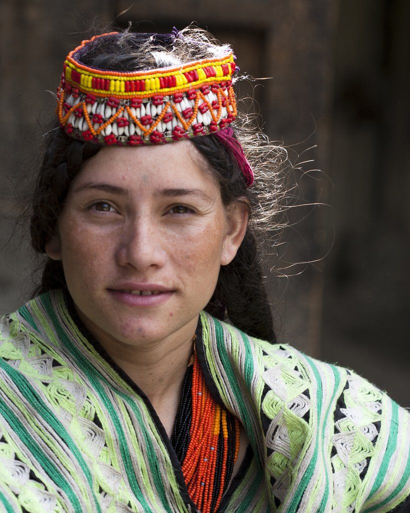 Portrait of a person wearing a colorful woven headpiece and striped shawl, looking at the camera