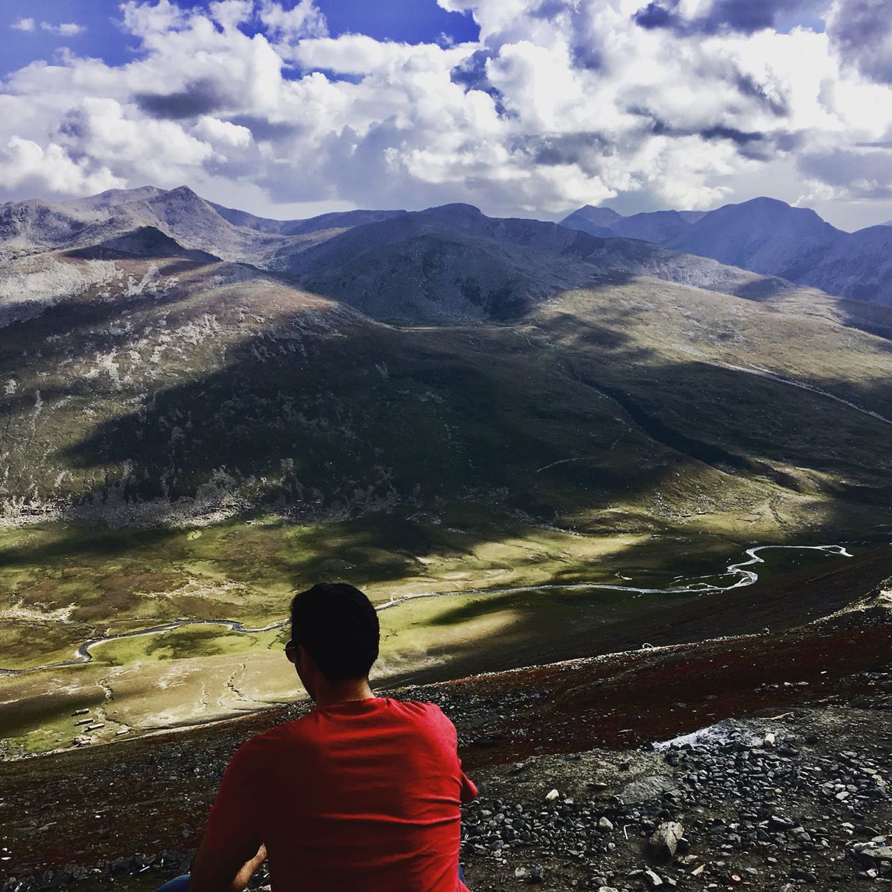 Person in a red shirt overlooking a mountain valley under cloudy skies