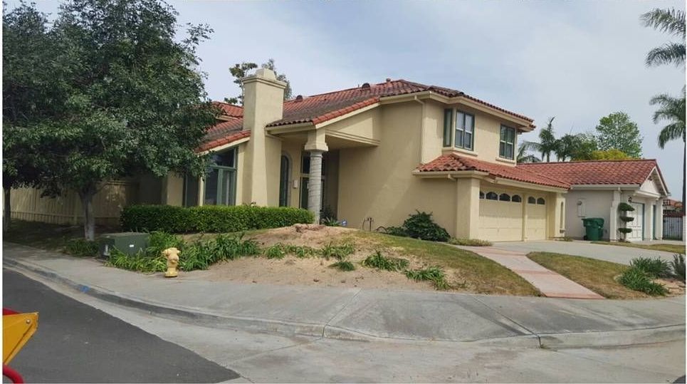 Two-story stucco house with red tile roof and three-car garage on a slight hill.