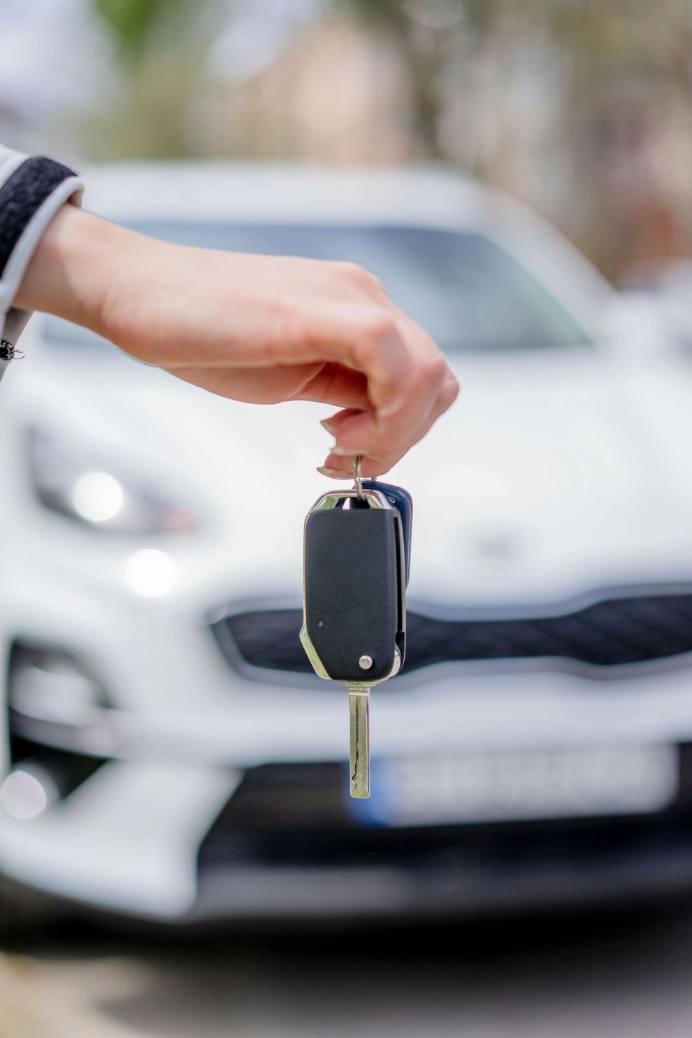 Mano che tiene il telecomando della chiave dell'auto davanti a un'auto bianca